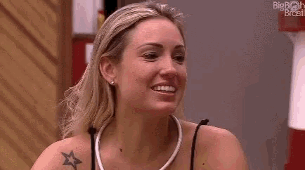 a woman with a tattoo on her shoulder is smiling and making a peace sign .
