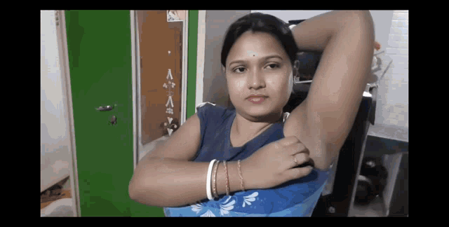 a woman in a blue shirt is looking at her armpit with a green door in the background