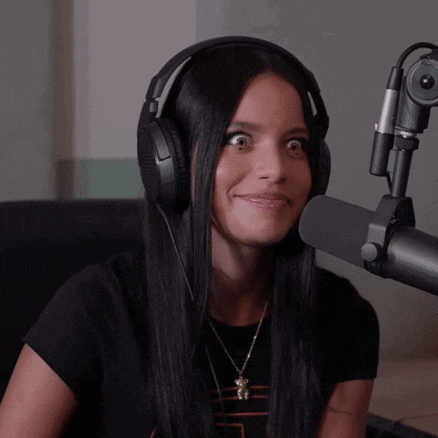 a woman wearing headphones stands in front of a microphone and making a funny face