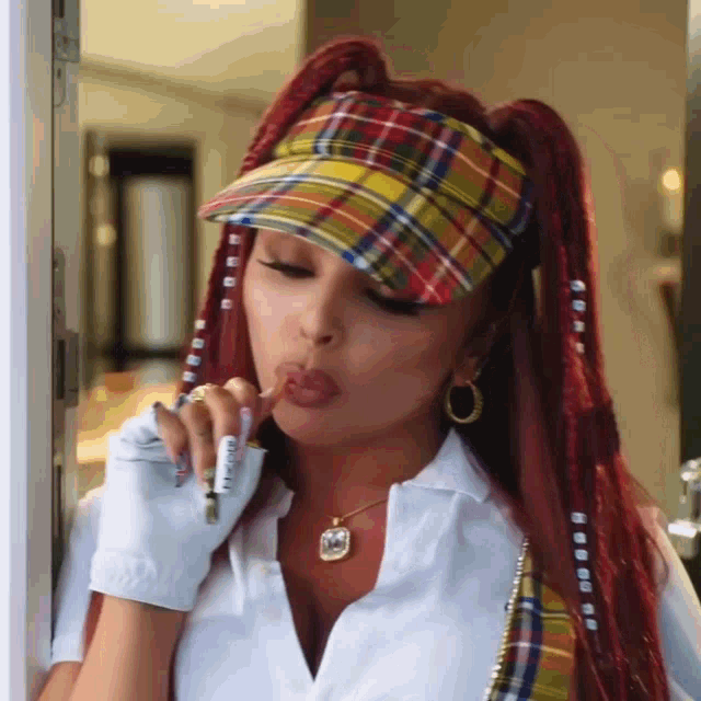 a woman wearing a plaid hat and a white shirt is blowing a cigarette out of her mouth