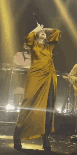 a woman in a yellow dress is kneeling down on a stage with a microphone in her hand .