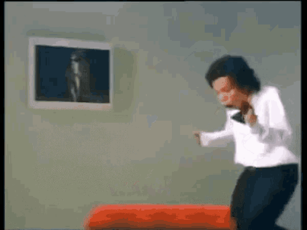 a man in a white shirt is dancing in front of a picture on the wall ..