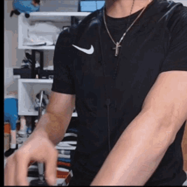 a man wearing a black nike shirt and a cross necklace is standing in a room .