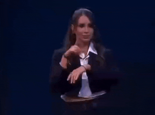 a woman in a suit and tie is sitting at a table in front of a black background .