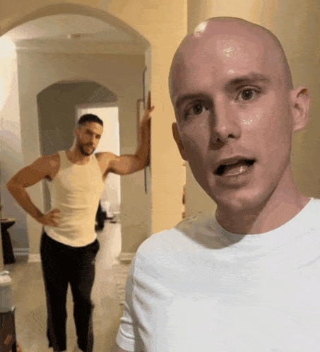 a bald man in a white shirt stands in front of another bald man