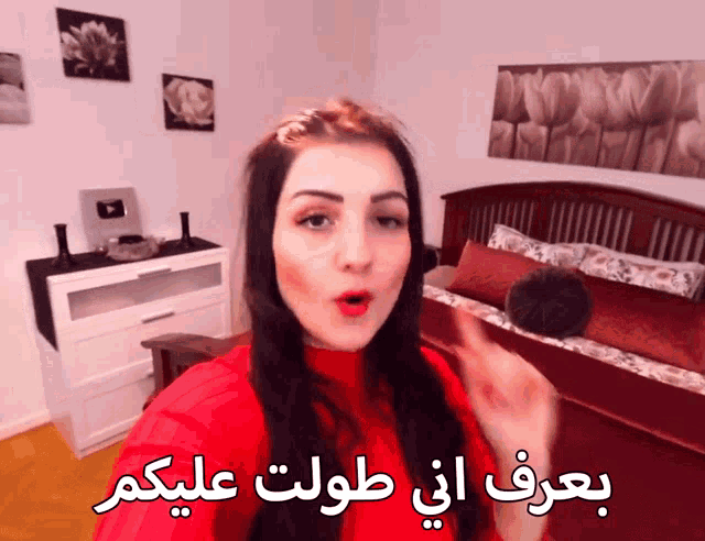 a woman in a red sweater stands in front of a bed with arabic writing on the bottom