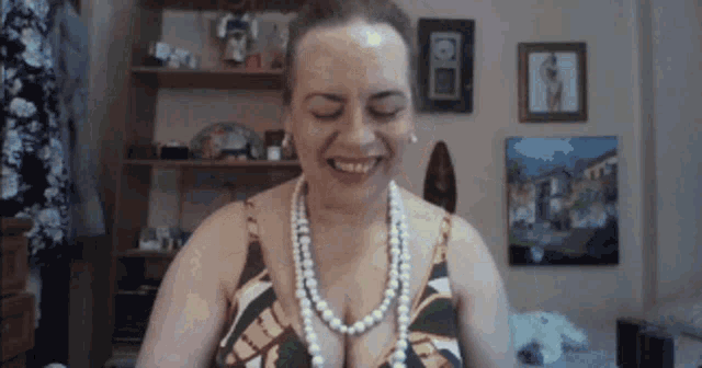 a woman wearing a pearl necklace is smiling with her eyes closed .