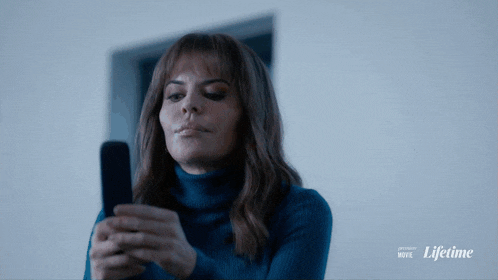a woman in a blue sweater is looking at her phone with the words lifetime movie behind her