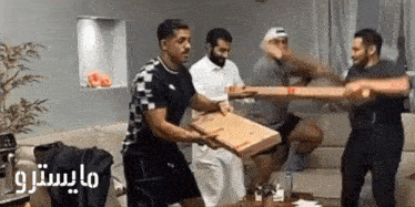 a group of men are holding a large pizza box in a living room .