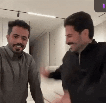 a couple of men are standing next to each other in a room and laughing .