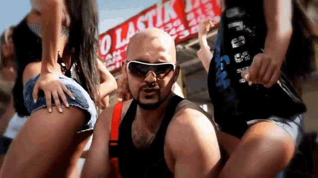 a bald man wearing sunglasses stands in front of a sign that says " olastik "