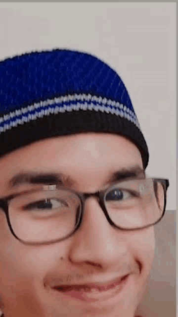 a man wearing glasses and a blue hat smiles for the camera .