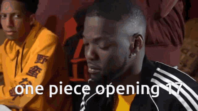 a man in a yellow shirt is sitting next to a man in a black jacket that says one piece opening 17