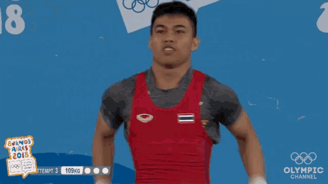 a man in a red tank top is standing in front of a sign that says ' olympic channel ' on it