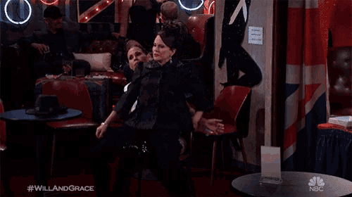 a woman is sitting in a chair with her arms outstretched in front of a table with a nbc logo on it