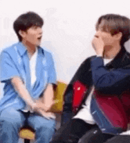 two men are sitting next to each other and talking . one of the men is covering his mouth with his hand .