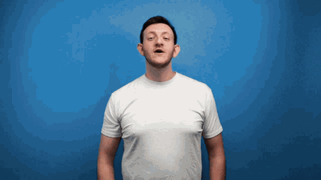 a man in a white t-shirt is standing in front of a blue wall