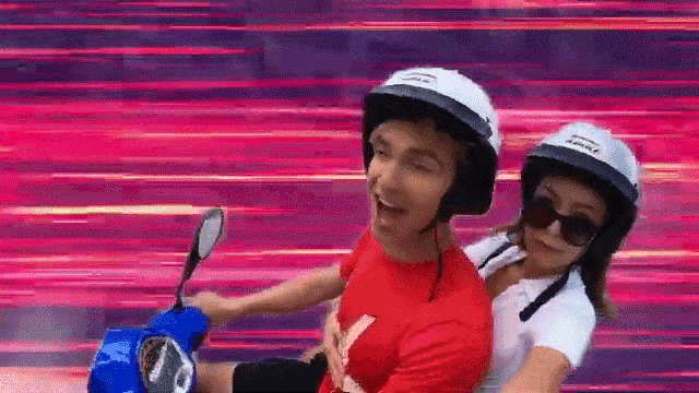 a man and a woman are riding a blue scooter with helmets on .