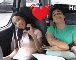a man and a woman are sitting in the back seat of a car with a heart in the background .