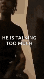 a man in a black shirt is standing in front of a wall and talking to someone .