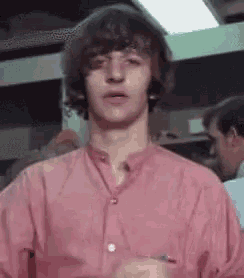 a young man in a pink shirt is standing in a room with other men .