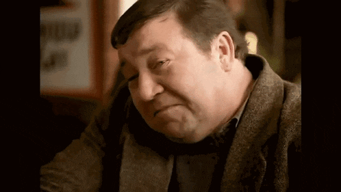 an older man is sitting at a table with his eyes closed and making a sad face .