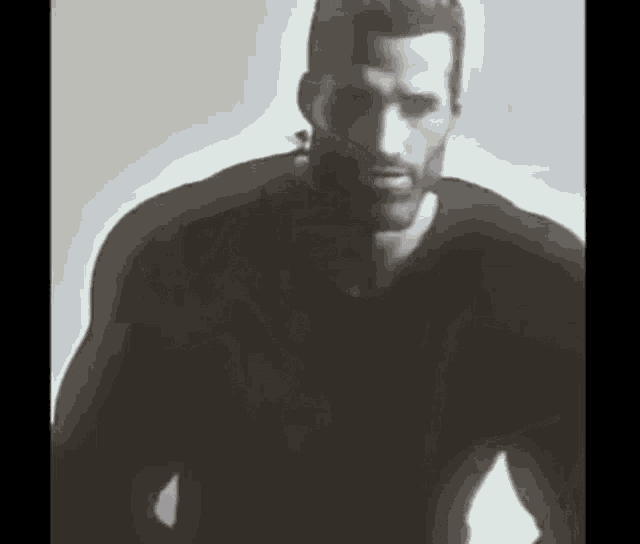 a black and white photo of a man with a beard wearing a black shirt and a headset .