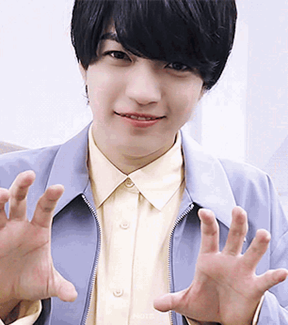 a young man wearing a blue jacket and a yellow shirt is making a hand gesture