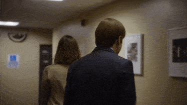 a man and woman are walking down a hallway with a handicap sign on the wall behind them
