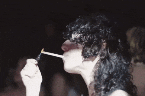 a woman with curly hair is lighting a cigarette