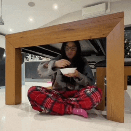 a woman is sitting under a table eating a bowl of cereal .