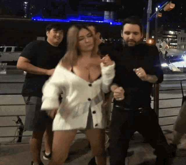 a woman in a white cardigan is dancing with two men in black shirts