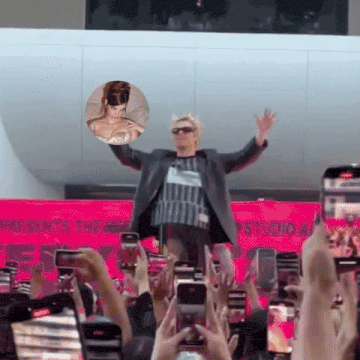 a man in a suit stands in front of a crowd of people taking pictures of him