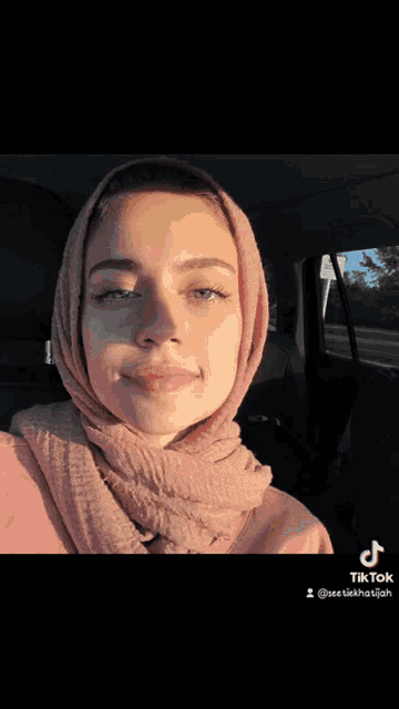 a woman wearing a black hijab with a ring on her finger is sitting in a car