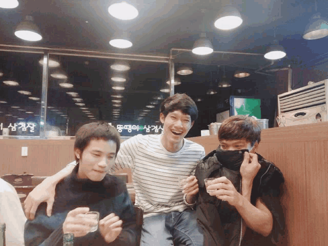 three young men are posing for a picture in a restaurant with a sign that says ' korean ' on it