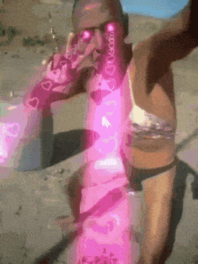 a woman in a bikini is standing on a beach with a pink light behind her