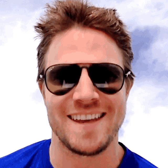 a man wearing sunglasses and a blue shirt smiles at the camera