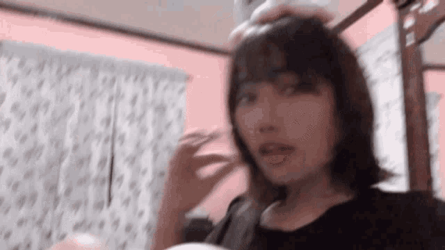 a woman with short hair is standing in a room with a pink wall and curtains .