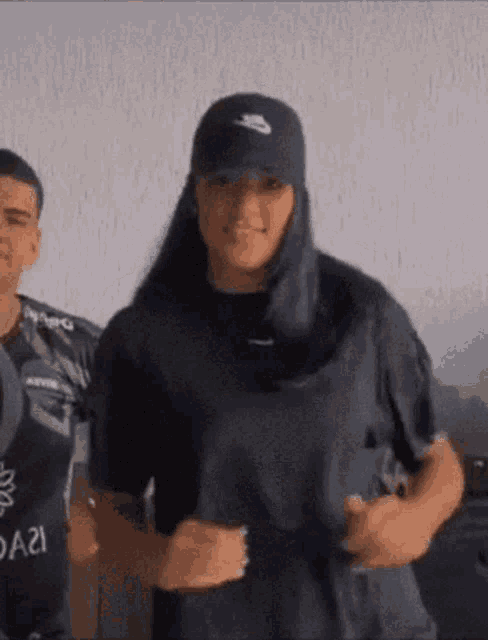 a man and a woman are standing next to each other . the woman is wearing a nike hat and a black shirt .