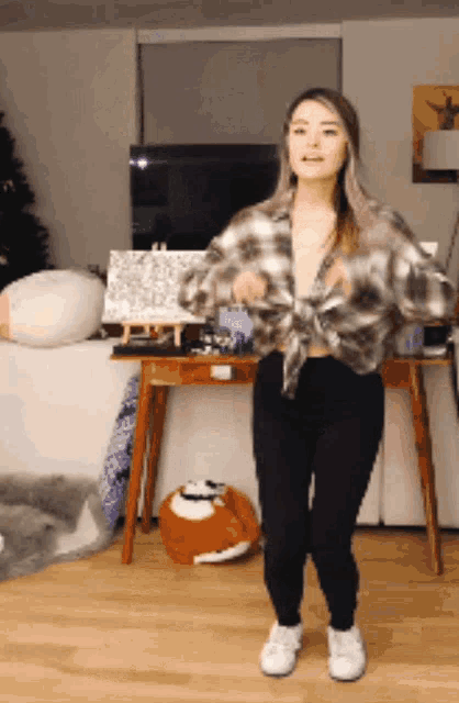 a woman wearing a plaid shirt and black pants is dancing in a living room