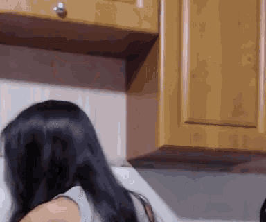 a woman with long black hair stands in front of a wooden cabinet