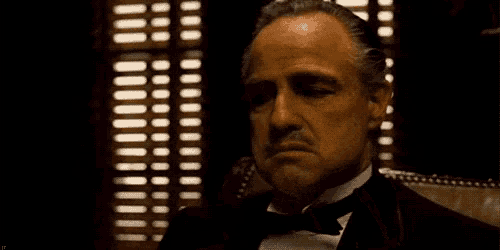 a man in a tuxedo is sitting in front of a window smoking a cigarette .