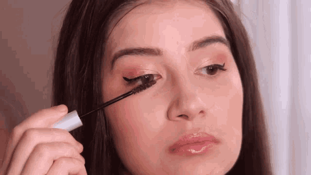 a woman is applying mascara to her eye with a brush .