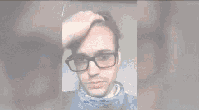 a man wearing glasses and a bandana is touching his hair .