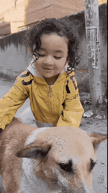 a little girl in a yellow jacket is petting a dog .