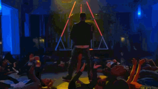a man in a black jacket stands on a stage in front of a crowd of people