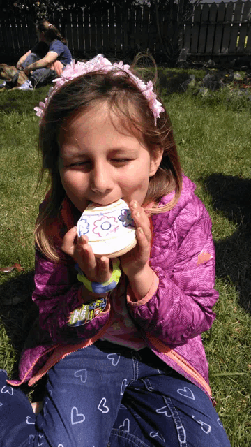 a little girl in a pink jacket is eating a cookie outside
