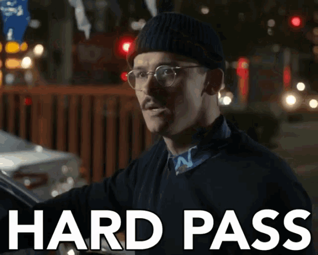 a man wearing glasses and a beanie is holding a car and says hard pass