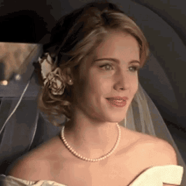 a bride wearing a pearl necklace and veil is smiling