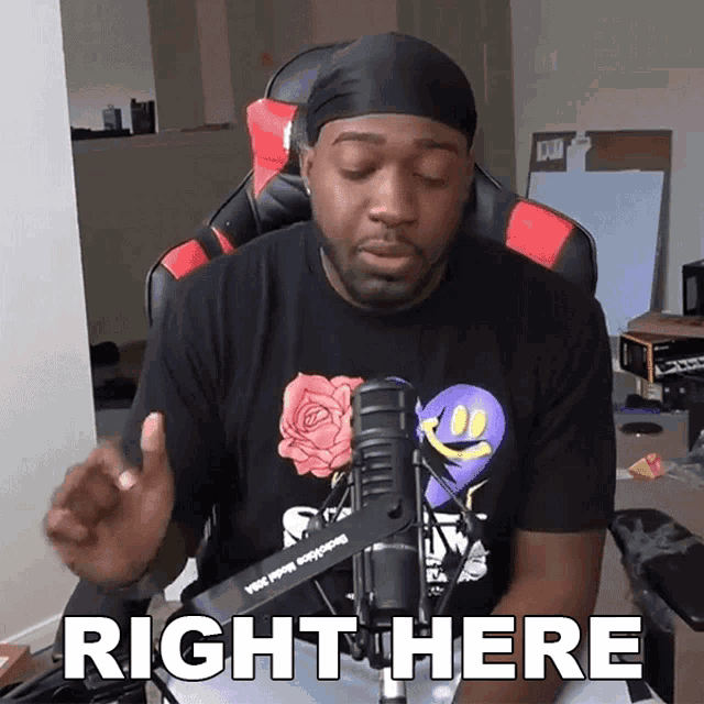 a man sitting in front of a microphone with the words right here on his shirt
